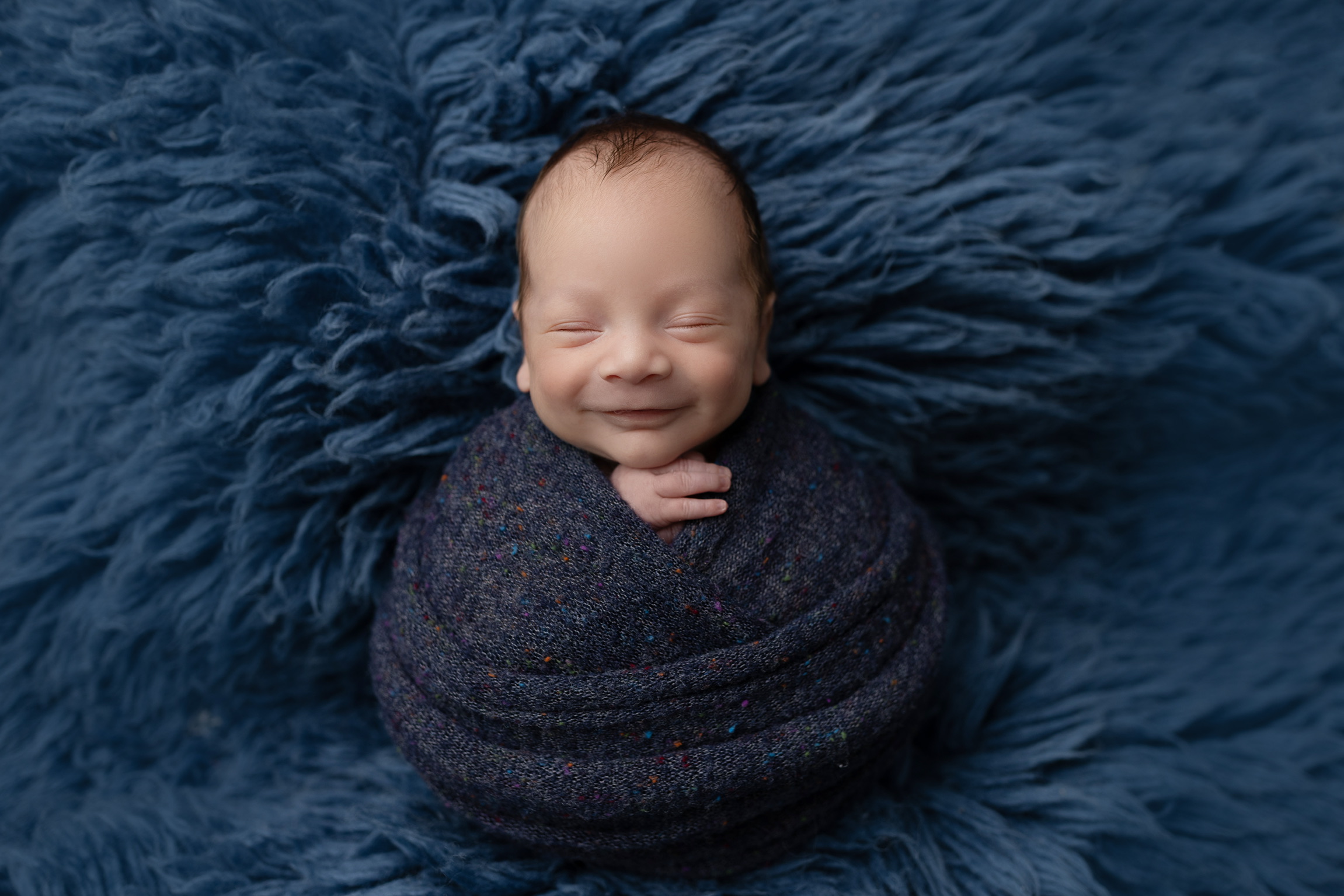 A smiling newborn baby boy supported by Blue Haven Ranch